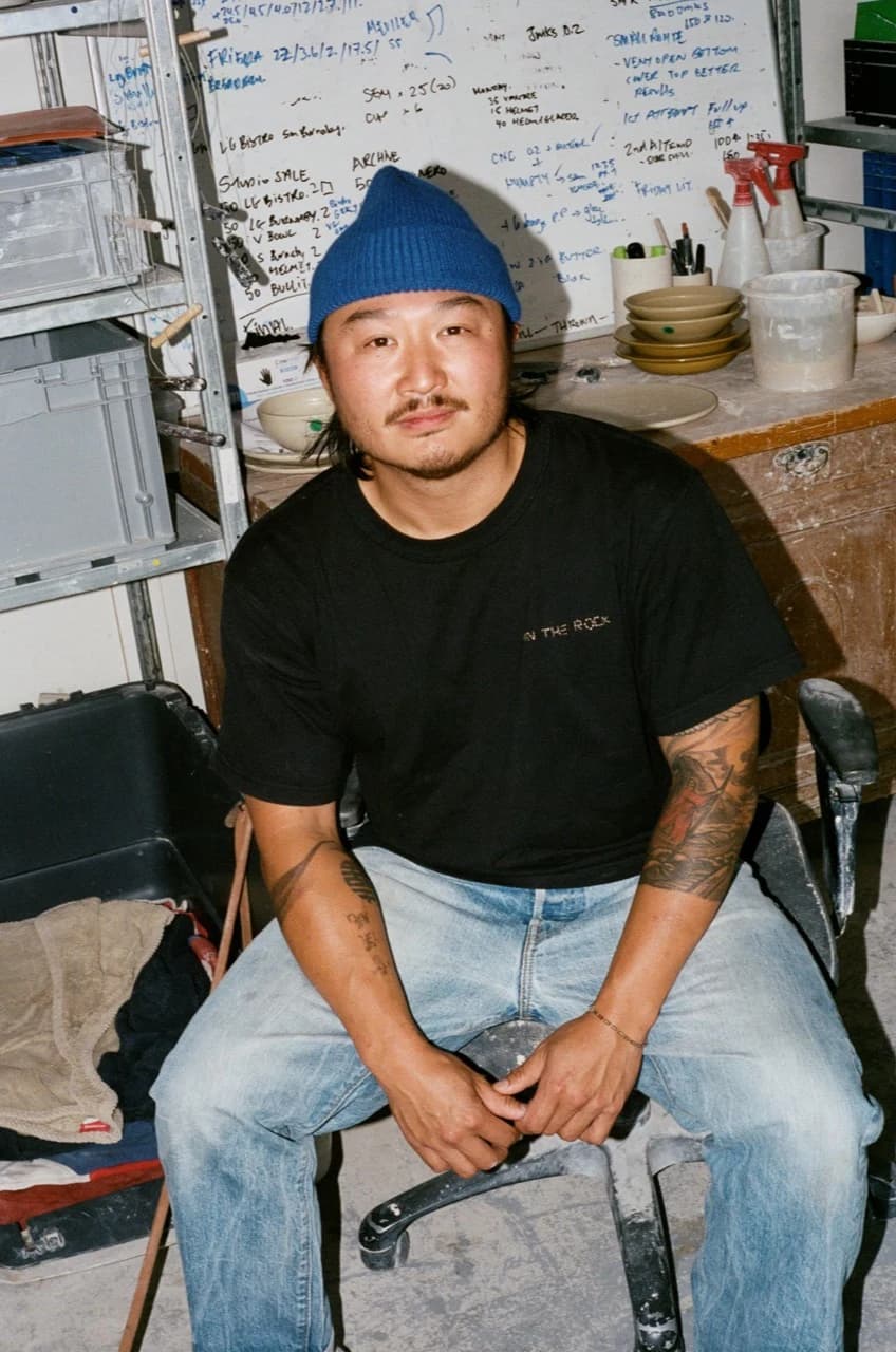 Johannes Tsang zit in zijn keramiekstudio met een blauwe beanie
