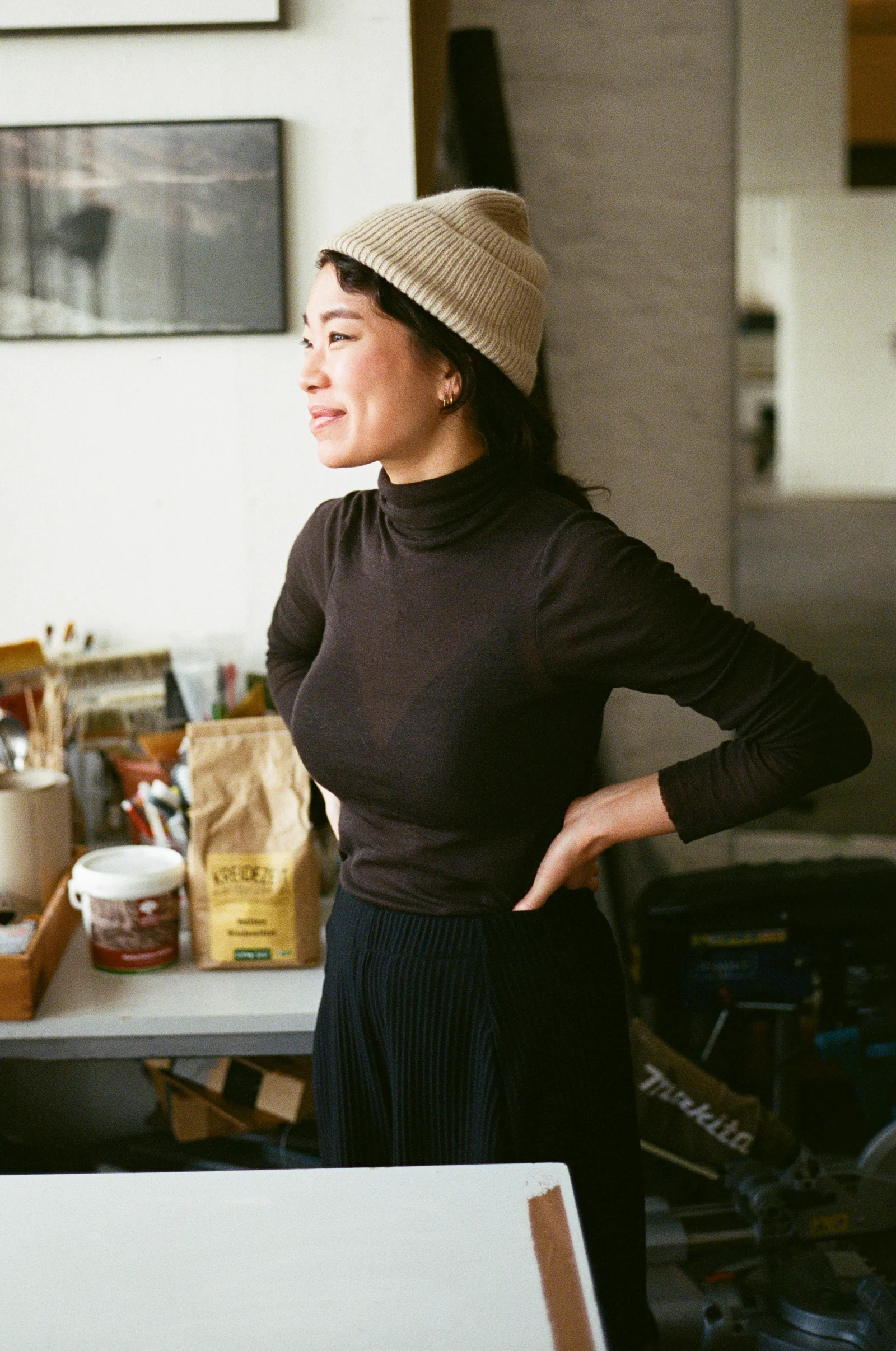Jeewi Lee in haar atelier met een crèmekleurige beanie en donkere coltrui