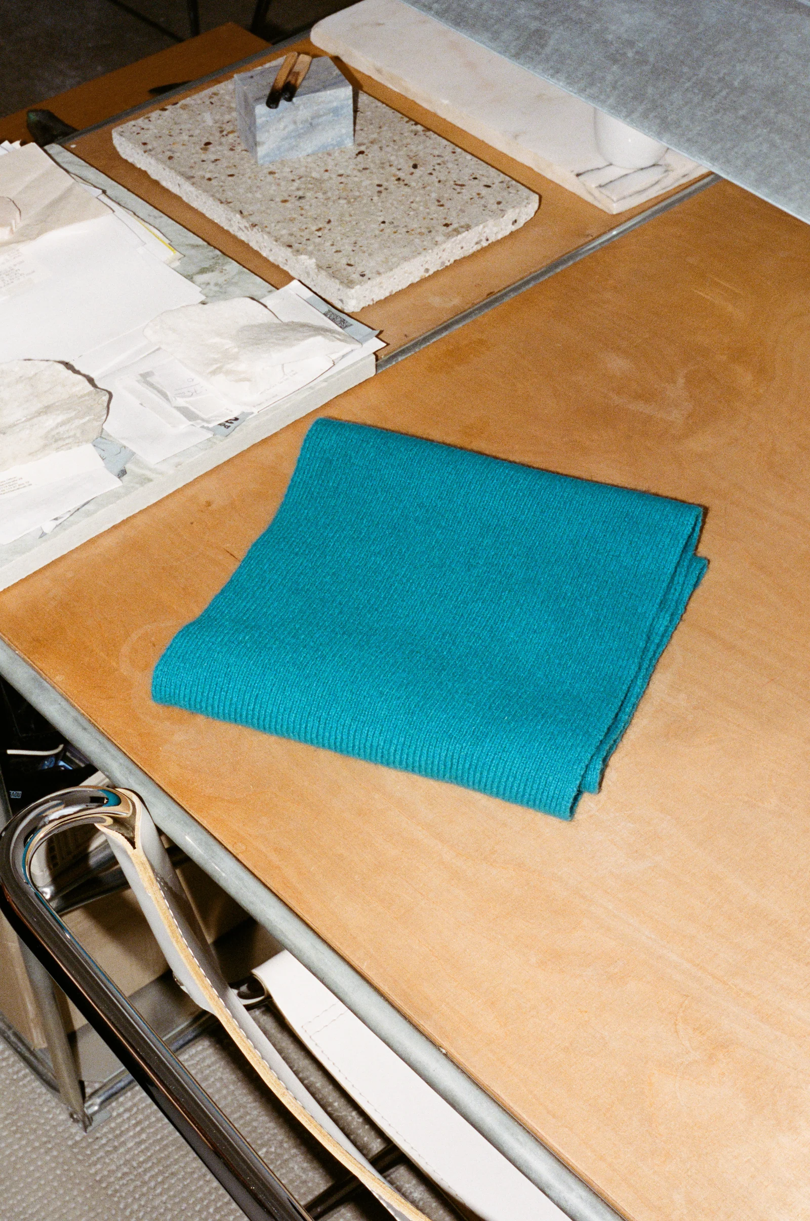 Een turquoise wollen sjaal naast papier en materiaalstalen op Jeewi Lees werktafel