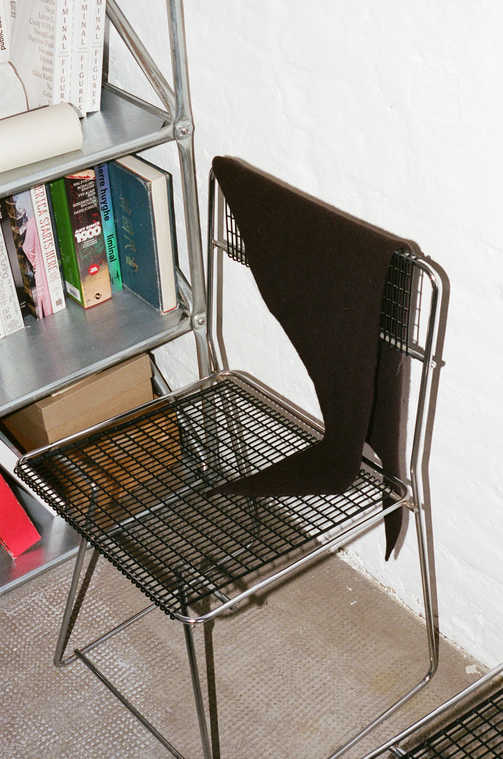 Een donkere wollen bandana op een draadstoel naast boeken in Jeewi Lees atelier