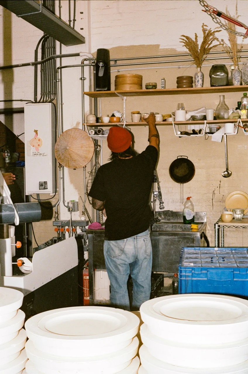 Johannes reaching for a cup in the studio kitchen, wearing a Terra beanie